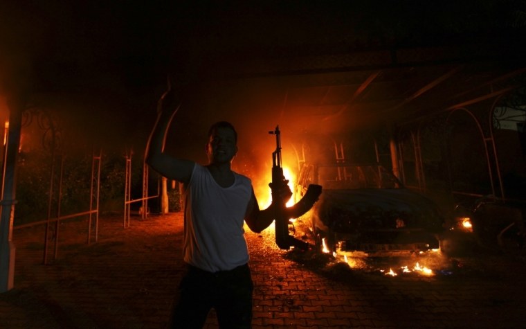 A protester reacts as the U.S. Consulate in Benghazi is seen in flames during a protest by an armed group said to have been protesting a film being produced in the United States September 11, 2012. An American staff member of the U.S. consulate in the eastern Libyan city of Benghazi has died following fierce clashes at the compound, Libyan security sources said on Wednesday. Armed gunmen attacked the compound on Tuesday evening, clashing with Libyan security forces before the latter withdrew as they came under heavy fire.