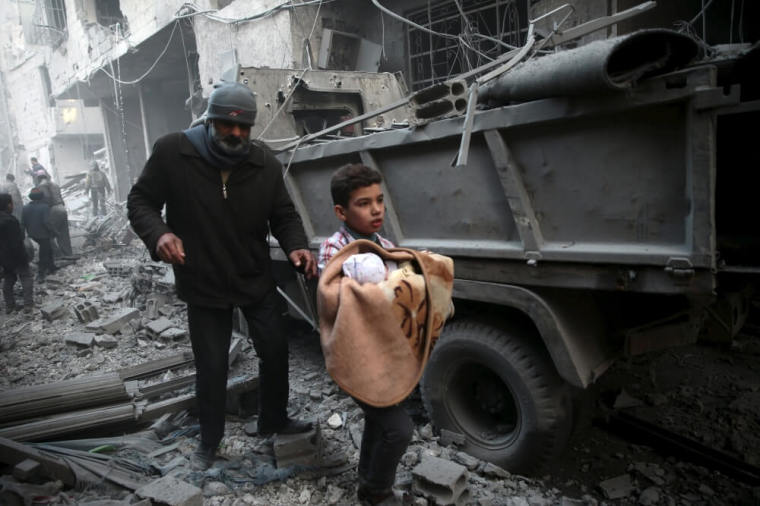 A boy carries a baby in a site hit by what activists said were airstrikes carried out by the Russian air force in the town of Douma, eastern Ghouta in Damascus, Syria, January 10, 2016.