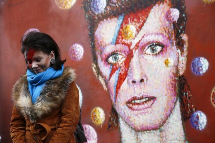 A woman wearing Ziggy Stardust style make-up reacts as she visits a mural of David Bowie in Brixton, south London, January 11, 2016. David Bowie, a music legend who used daringly androgynous displays of sexuality and glittering costumes to frame legendary rock hits 'Ziggy Stardust' and 'Space Oddity', has died of cancer.