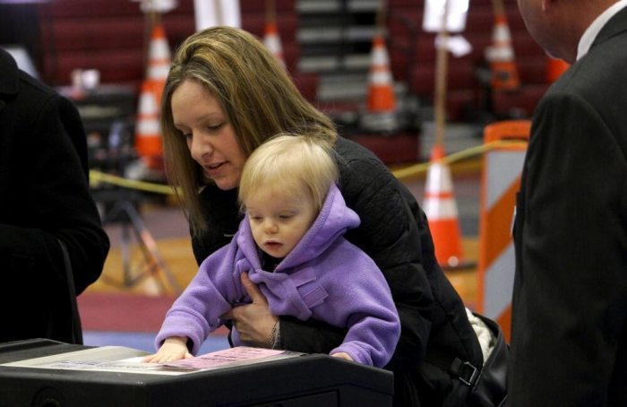A woman has her child push her ballot into the tabulation machine as she votes in the presidential primary at Bedford High School in Bedford, New Hampshire, February 9, 2016.
