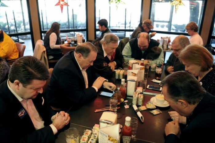 U.S. Republican presidential candidate Mike Huckabee (2nd L) prays before lunch with supporters at Drake Diner in Des Moines, Iowa February 1, 2016.