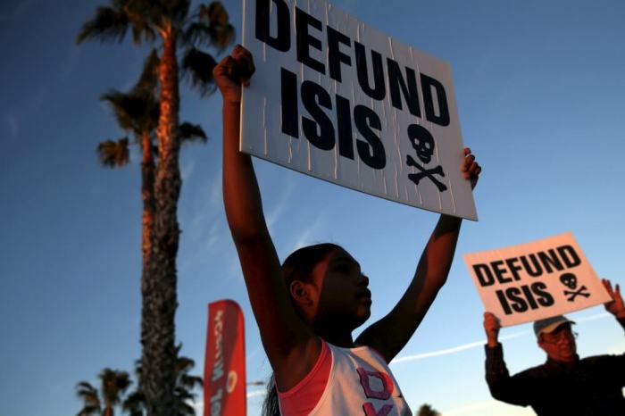 People protest against ISIS across from a makeshift memorial for victims of the San Bernardino shooting, ahead of President Obama's visit with the victims' families in San Bernardino, California, on December 18, 2015.