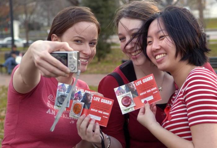 Amanda Dachille, Jamie Bright and Julie Phung (L-R) pose with handout condoms and take a picture of themselves as they gathered at a World AIDS Day rally near the White House in Washington, December 1, 2006.