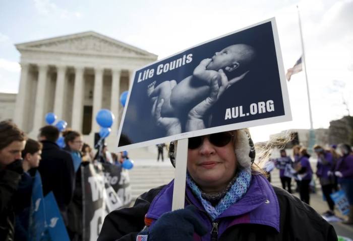 A protester holds up a sign in front of the U.S. Supreme Court on the morning the court takes up a major abortion case focusing on whether a Texas law that imposes strict regulations on abortion doctors and clinic buildings interferes with the constitutional right of a woman to end her pregnancy, in Washington March 2, 2016.