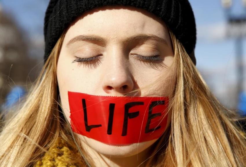 A protester with her mouth taped over with the word "life" stands in front of the U.S. Supreme Court.