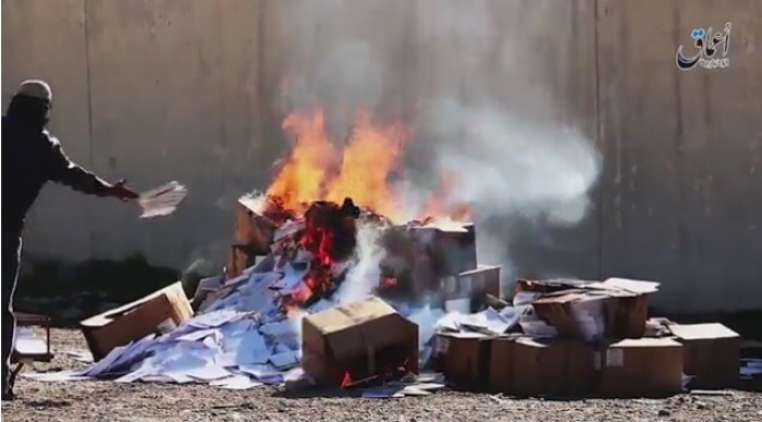 An Islamic State militant tosses Christian textbooks into a bonfire on the grounds that they are the 'books of infidels' on March, 10 2016.