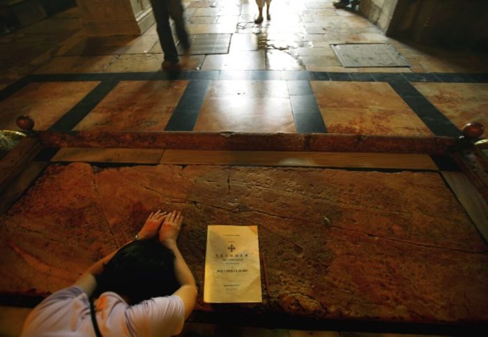 A Christian pilgrim prays at the large marble slab traditionally believed to be the stone that Jesus Christ's body was washed upon when removed from the cross, in the Church of the Holy Sepulcher, Jerusalem, Israel.