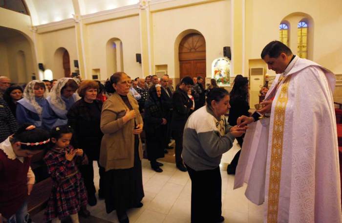 A priest gives communion to an Iraqi Christian woman, during mass at Mar George Chaldean Church in Baghdad, March 1, 2015. Iraqi Christians say they have no intention of leaving the country despite the recent abduction of over 100 Assyrian Christians by the Islamic State. Picture taken March 1, 2015.