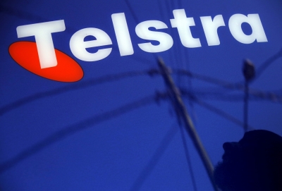 A man and power lines are reflected in a Telstra poster adorning a public telephone in Sydney, Australia, August 13, 2015.