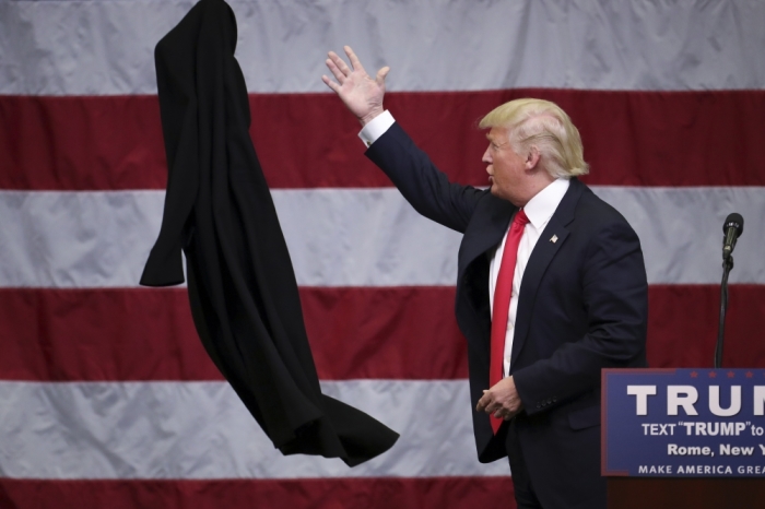 U.S. Republican presidential candidate Donald Trump tosses off his overcoat as he speaks at a campaign event in an airplane hangar in Rome, New York April 12, 2016.