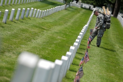 A soldier of the 3rd U.S. Infantry Regiment (The Old Guard) places flags in front of the graves at Arlington National Cemetery in Washington.