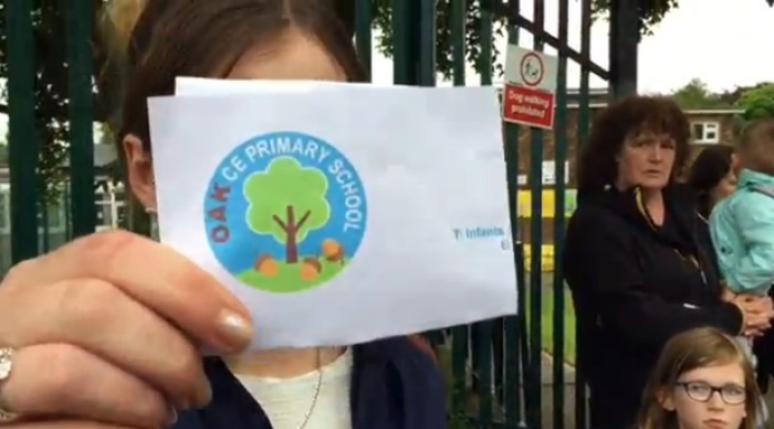 A parent participates in a protest outside of the holds up the new version of the Oak CE Primary School in Huddersfield, West Yorkshire to protest the removal of a cross from the school's logo.