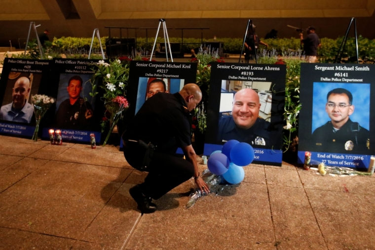 A Dallas police officer picks up balloons and flowers in front of images of the 5 slain officers after a candlelight vigil at Dallas City Hall following the multiple police shootings in Dallas, Texas, July 11, 2016.