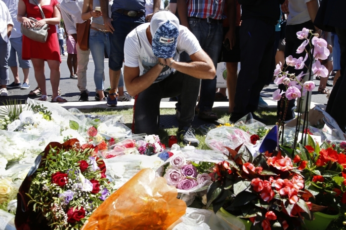 A man reacts near bouquets of flowers as people pay tribute near the scene where a truck ran into a crowd at high speed killing scores and injuring more who were celebrating the Bastille Day national holiday, in Nice, France, July 15, 2016.