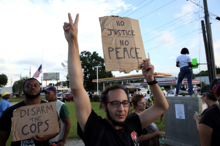 Protesters hold signs reading 'No justice, no peace,' and 'Disarm the cops' as they protest the killing of Alton Sterling by police officers in Baton Rouge, Louisiana, July 16, 2016.