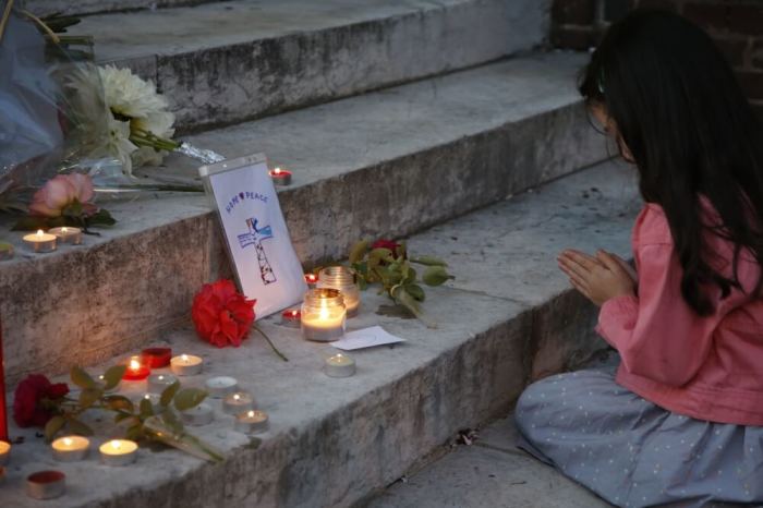 A young girl prays near flowers and candles at the town hall in Saint-Etienne-du-Rouvray, near Rouen in Normandy, France, to pay tribute to French priest, Father Jacques Hamel, who was killed with a knife and another hostage seriously wounded in an attack on a church that was carried out by assailants linked to Islamic State, July 26, 2016.