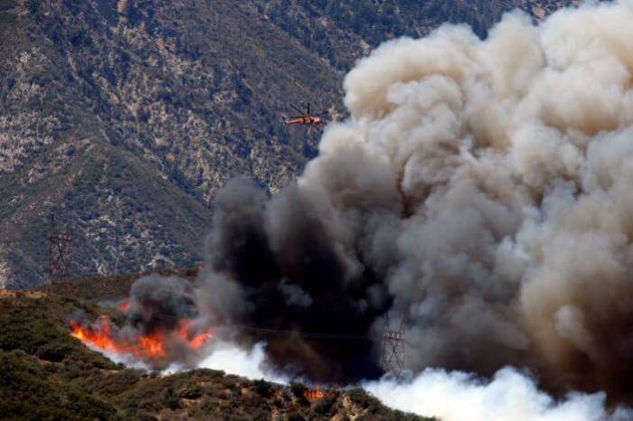 A firefighting helicopter maneuvers around power lines and smoke to make a water drop during the Blue Cut fire at the Cajon Pass in San Bernardino County, California, U.S. August 17, 2016.