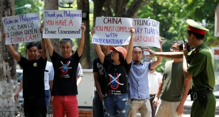 A policeman tries to stop anti-China protesters holding placards during a demonstration in front of the Philippines embassy in Hanoi, Vietnam, July 17, 2016.