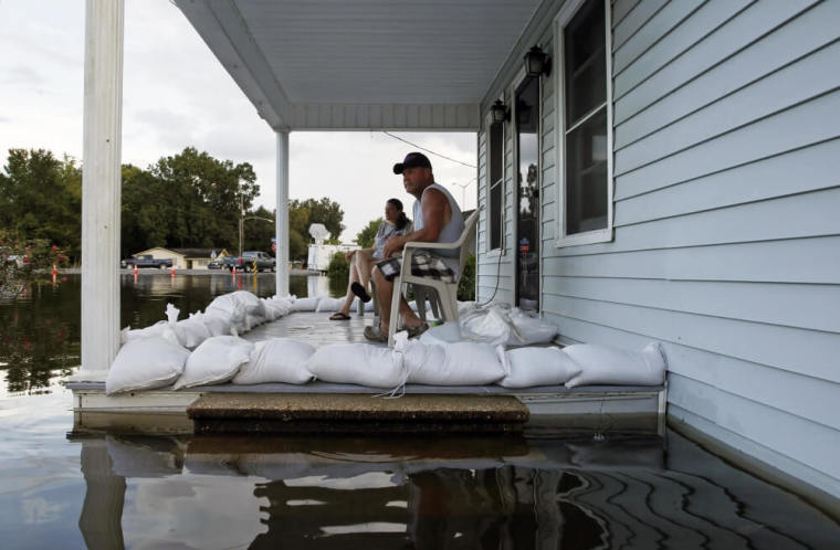 Megan Schexnayder and David McNeely (R) sit on the porch of a home which is surrounded by floodwaters after heavy rains in Sorrento, Louisiana, August 17, 2016.