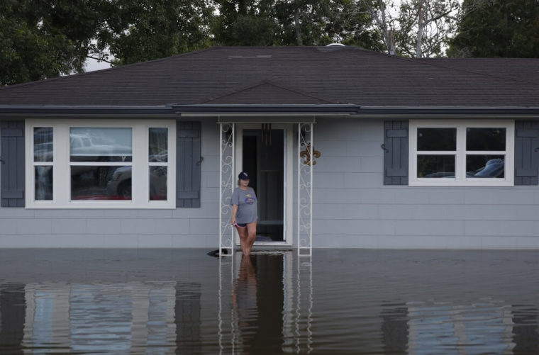 A woman smokes a cigarette on the front porch of a home surrounded by floodwaters in Sorrento, Louisiana, August 17, 2016.
